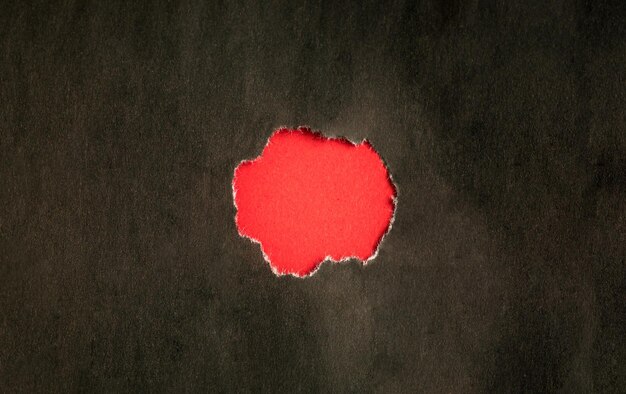 Torn black hole on red paper background
