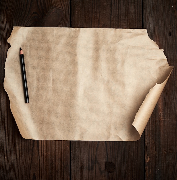 Photo torn empty sheet of brown paper and a black pencil on a wooden surface from old boards