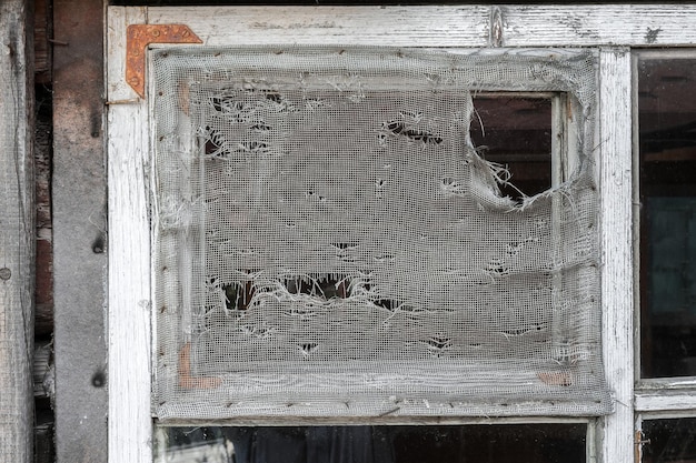 A torn mosquito net on an old wooden window frame of a village house