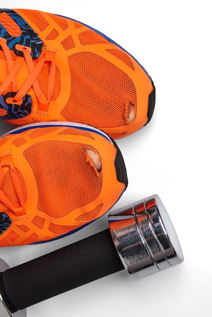 Torn orange sneakers with protruding toes and a metal dumbbell isolated on a white background