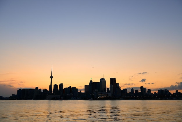 Toronto city skyline silhouette at sunset over lake with urban skyscrapers.