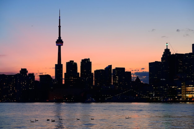 Toronto city skyline silhouette at sunset over lake with urban skyscrapers.