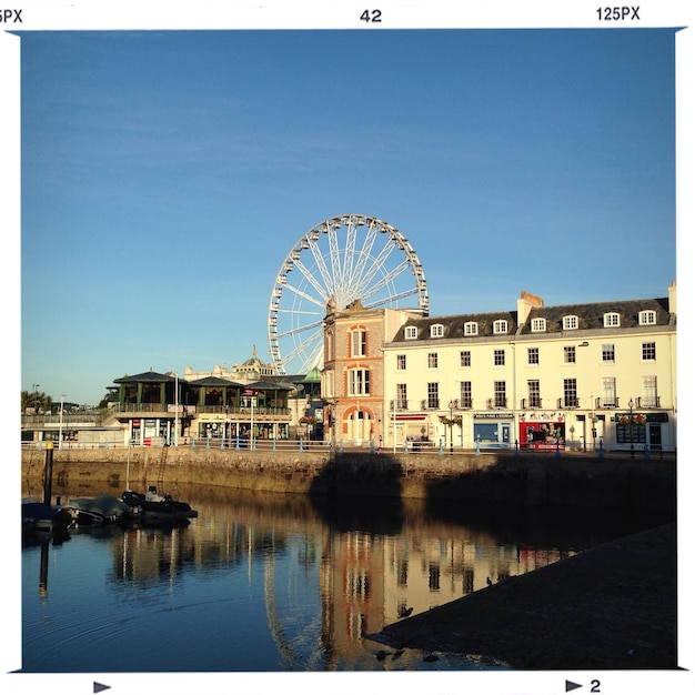 Torquay harbor by city buildings and ferris wheel against sky