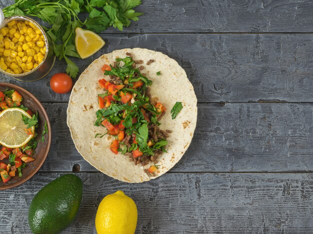 Tortilla cooking Mexican Taco, vegetarian salad, lemon, parsley, avocado and spices on a dark wooden table