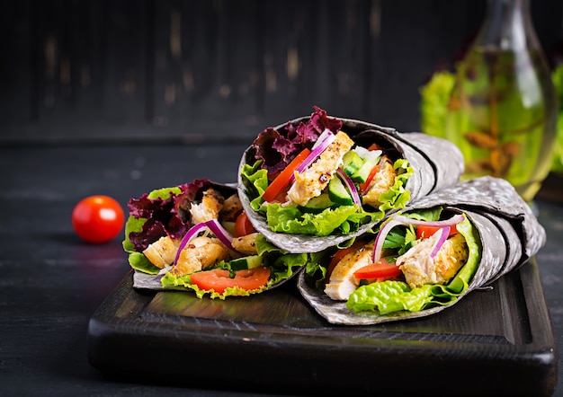 Tortilla con involucri di seppia di inchiostro aggiunto con pollo e verdure su superficie nera. burrito di pollo, cibo messicano.