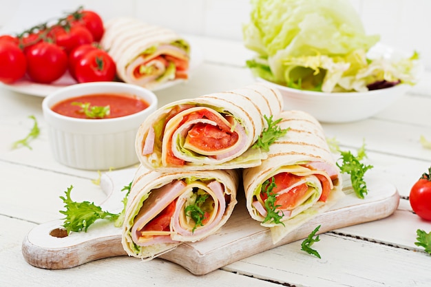 Tortilla wrap met ham, kaas en tomaten op een witte houten tafel