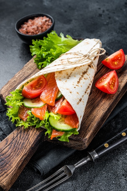 Tortilla Wrap salmon roll with salad, vegetables. Black background. Top view.