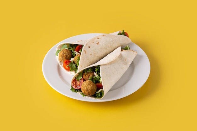 Tortilla wrap with falafel and vegetables on yellow background