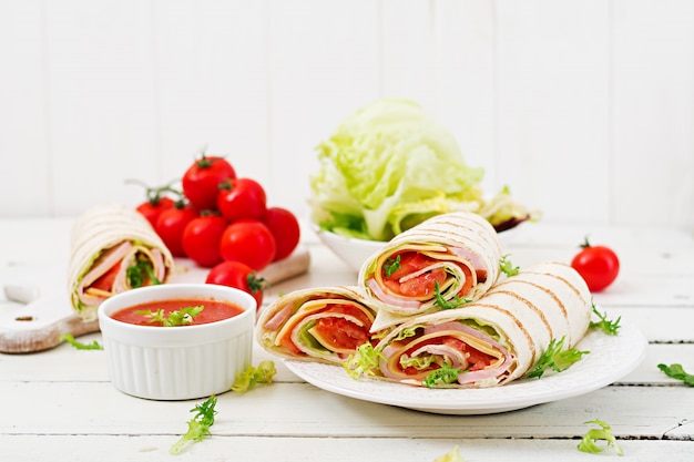 Tortilla wrap with ham, cheese and tomatoes on white wood