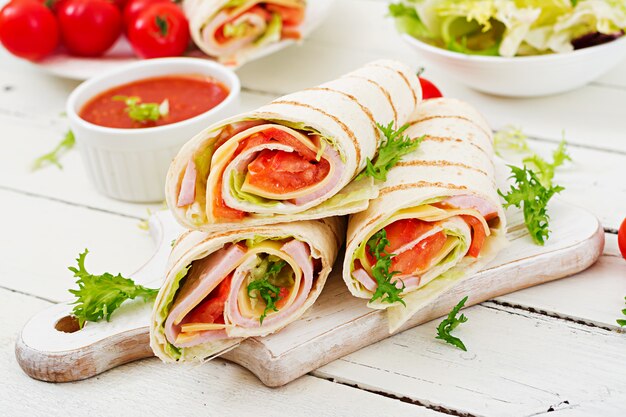 Tortilla wrap with ham, cheese and tomatoes on white wood