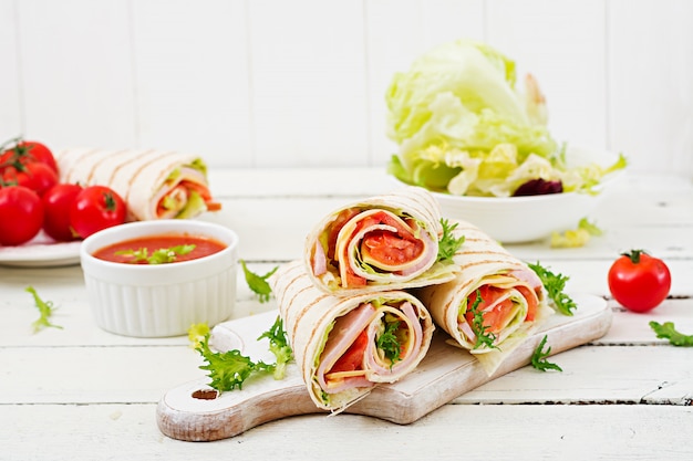 Foto involucro della tortiglia con prosciutto, formaggio e pomodori su legno bianco