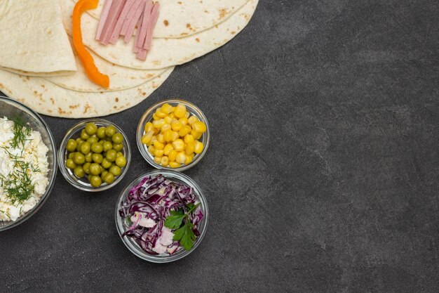 Foto imballaggi di tortilla e riempimento di verdure per tortilla in ciotole di vetro sfondo nero piatto