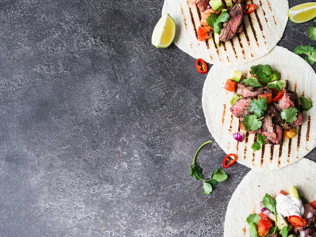 Tortillas with vegetables and beef steak slices. Avocados, tomatoes, red onions and meet with cilantro and lime juice in tortillas. Mexican food.