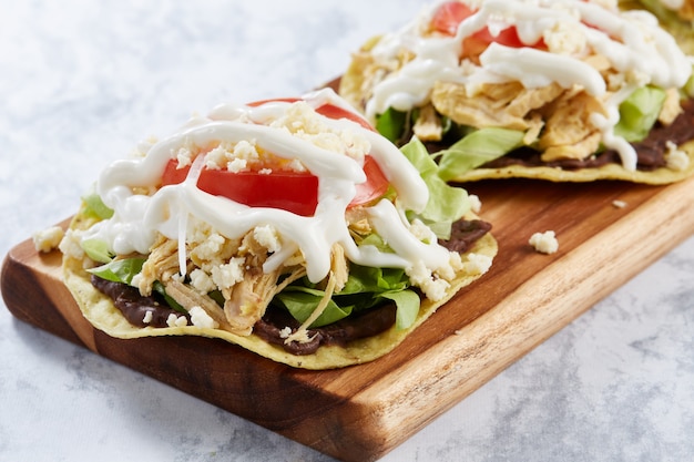 Tostadas de pollo con base de frijoles lechuga tomate queso y crema