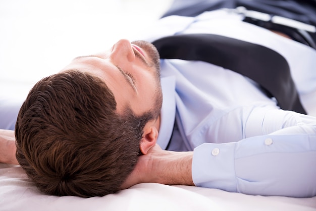 Totale ontspanning. Achteraanzicht van een jonge man in overhemd en stropdas, hand in hand achter het hoofd terwijl hij in bed slaapt