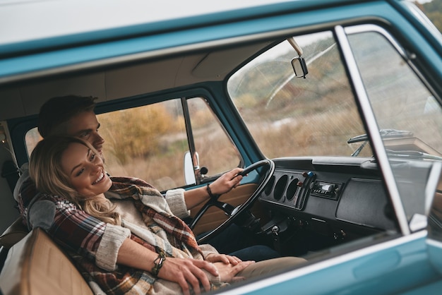 Totalmente felice. bella giovane coppia che si abbraccia e sorride mentre è seduta in un mini furgone blu in stile retrò