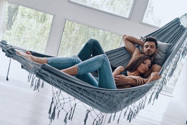 Totally in love. Beautiful young couple embracing while sleeping in the hammock indoors