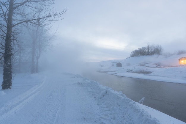 完全に雪に覆われた道と、蒸気のある雪景色の中で黄色い光を放つアイスランドの温室