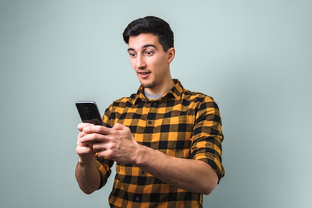 Totally surprised man in yellow square shirt looking into the phone