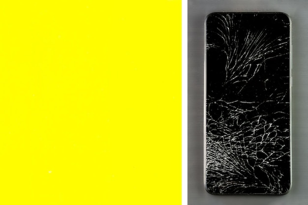 A touch phone with a broken screen lies on a gray metal brushed surface Layout with space for copying yellow color