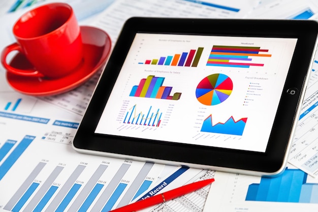 Touch screen tablet computer with charts on screen and cup on table