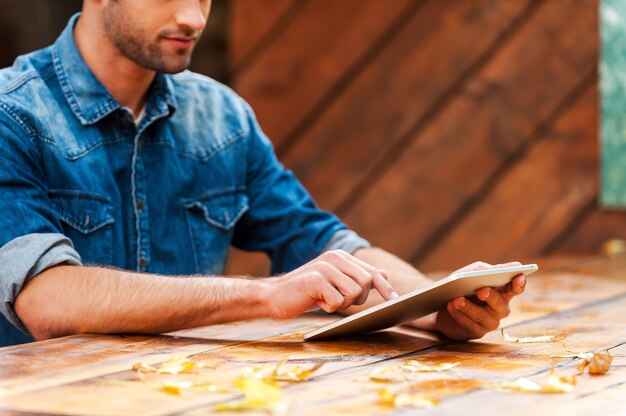 Touch-technologie. Bijgesneden afbeelding van jonge man aan het werk op digitale tablet zittend aan de houten tafel buiten