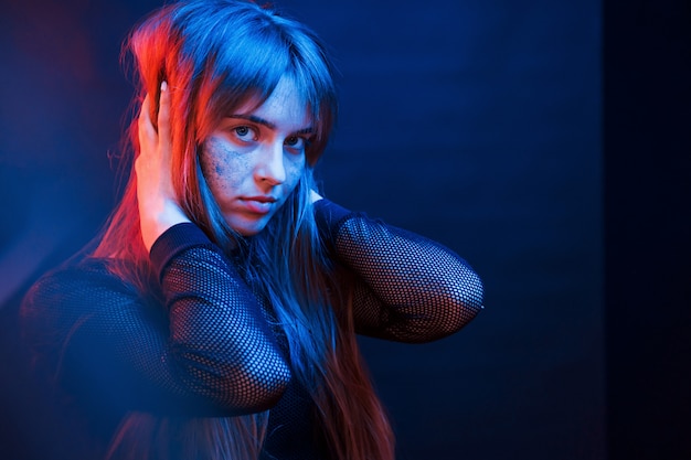 Touching beautiful hair. Studio shot in dark studio with neon light. Portrait of young girl