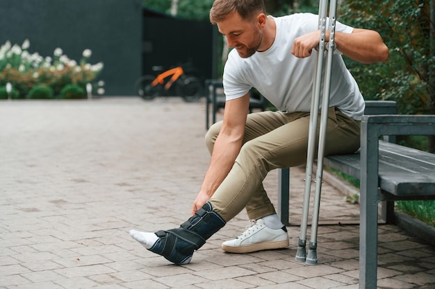 Touching the leg Man with crutches is in the park outdoors