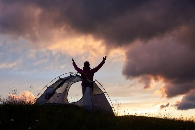 空に触れる。山で素晴らしい夕日を楽しんでいる空に手を持ち上げる女性登山家