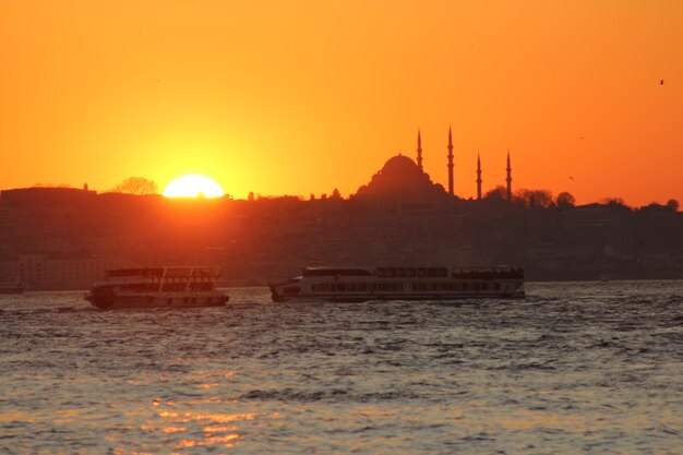 Tourboats in river by silhouette suleymaniye mosque against sky during sunset