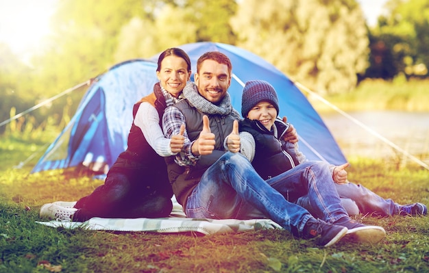 Photo tourism, hike and travel concept - happy family over tent at camp site showing thumbs up gesture