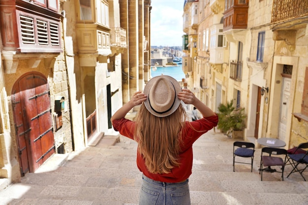 Tourism in Malta Back view of tourist girl holding hat descends stairs in the old town of Valletta UNESCO World Heritage Malta