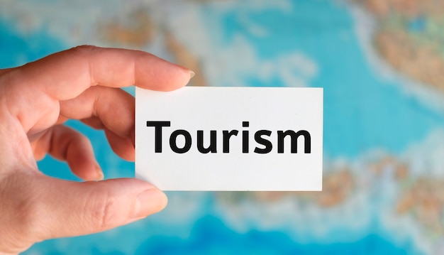 Туризм - текст на белом листе с глобусом на фоне карты атласа