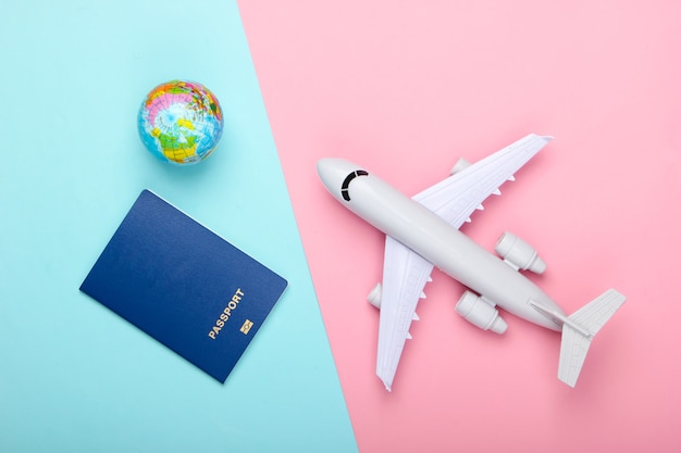 Tourism and travel concept. Emigration. Globe,  passport and passenger plane figurine on pink blue pastel wall Top view. Flat lay