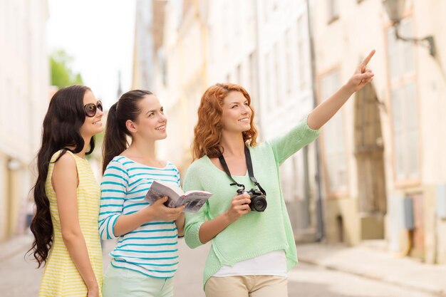 Photo tourism, travel, leisure, holidays and friendship concept - smiling teenage girls with city guide and camera outdoors