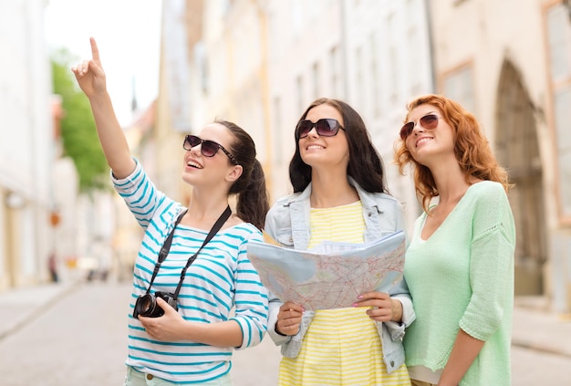 tourism, travel, leisure, holidays and friendship concept - smiling teenage girls with map and camera outdoors