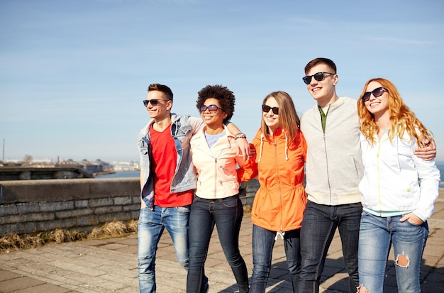 tourism, travel, people and leisure concept - group of happy teenage friends walking along city street