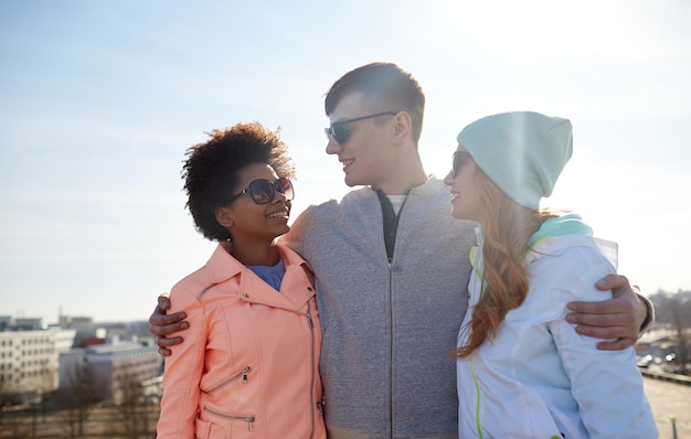 Turismo, viaggi, persone, tempo libero e concetto adolescenziale - gruppo di amici felici in occhiali da sole che si abbracciano e parlano sulla strada della città