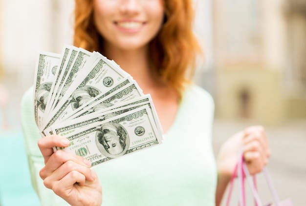 Photo tourism, travel, sale and consumerism concept - close up of happy woman with shopping bags and dollar money on city street