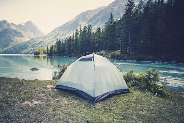 Tourism and traveling concept beautiful summer landscape with\
mountains and tourist tent green tent stands near the lake in the\
mountains