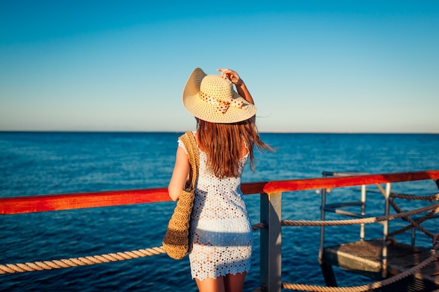 Tourism. Young woman traveler admiring landscape on pier by Red sea. Summer fashion