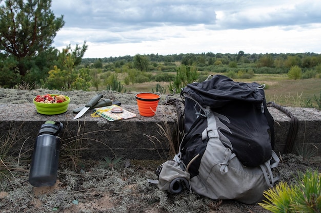 Tourist backpack and tableware in nature A snack of a tourist on a camping trip Knife and dishes