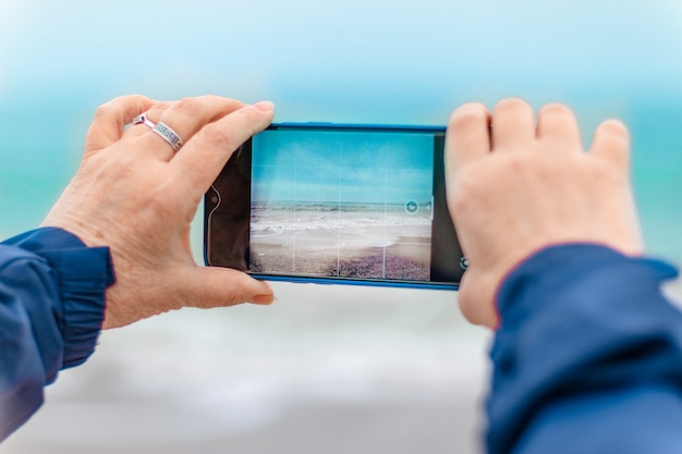 観光白人女性の手がビーチで携帯電話で海の写真を撮る旅行休暇の概念