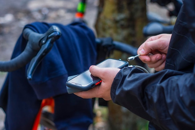 관광객은 자연에서 자전거를 배경으로 보조 배터리가 있는 스마트폰을 충전합니다.