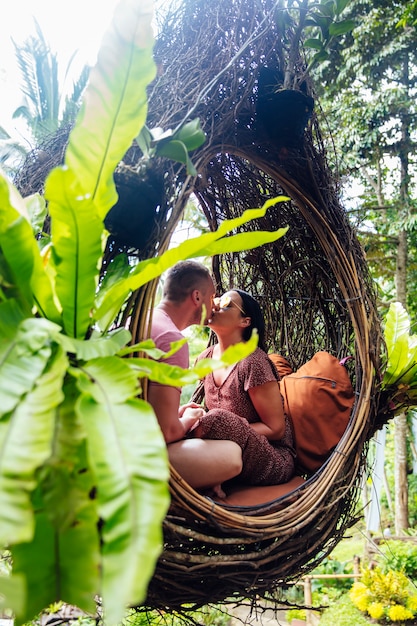 A tourist couple sitting on a large bird nest on a tree at Bali island