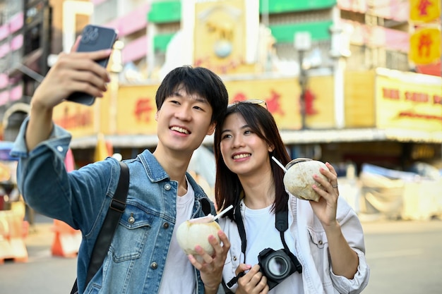 A tourist couple taking a photo or selfie with a smartphone in a Chinatown