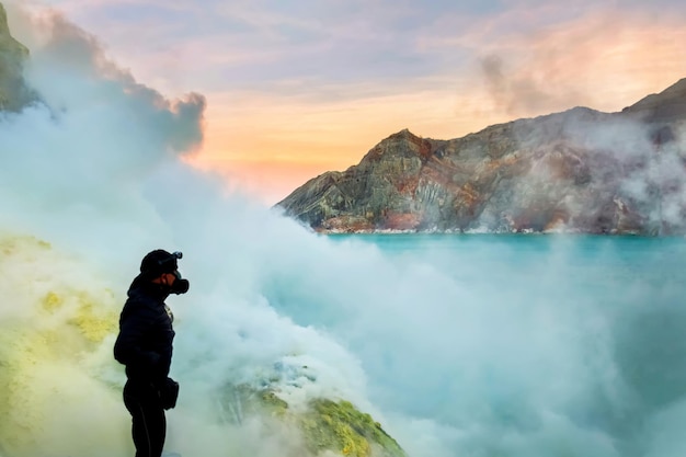 火山の火口の観光客硫黄は火山の青い湖とピンクの夜明けをペアにします活火山の口への危険な旅グヌンイジェンインドネシアジャワ島