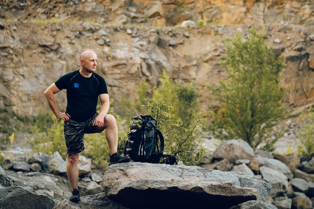 A tourist dressed in sportswear is leaning with his right leg on the stone on the background of rocks A traveler poses for a photo shoot in memory of the current journey