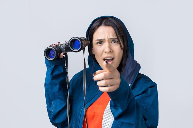 Una ragazza turistica con un impermeabile blu tiene in mano un binocolo e guarda lontano, spie.