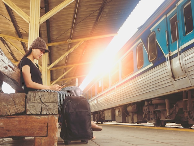 Туристическая девушка играет сотовый телефон в ожидании поезда